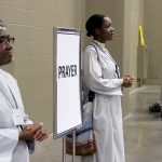 Two women stand, ready to assist prayerful conventioners