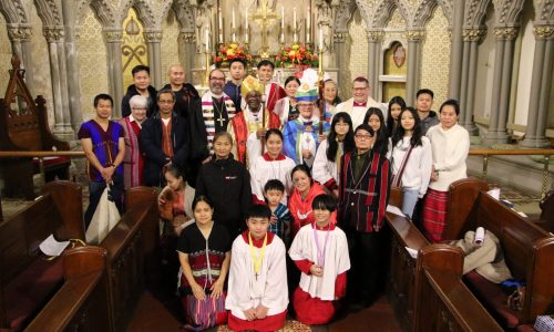 Image Description: A group of Karen families from Grace Episcopal Church in Utica, NY pose in the sanctuary of the church in front of the altar with Presiding Bishop Michael Curry, Bishop DeDe Duncan-Probe, Bishop Lee Miller II of the Upstate NY Synod of the ELCA, and Bishop Douglas Lucia of the Roman Catholic Diocese of Syracuse after a diocesan event in December of 2023.